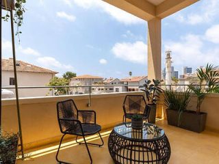 Balcony view with two black chairs and a table, overlooking traditional white buildings and a distant minaret.